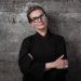 Skilled female chef with glasses, confident pose, dark kitchen uniform, inspiring culinary professional.