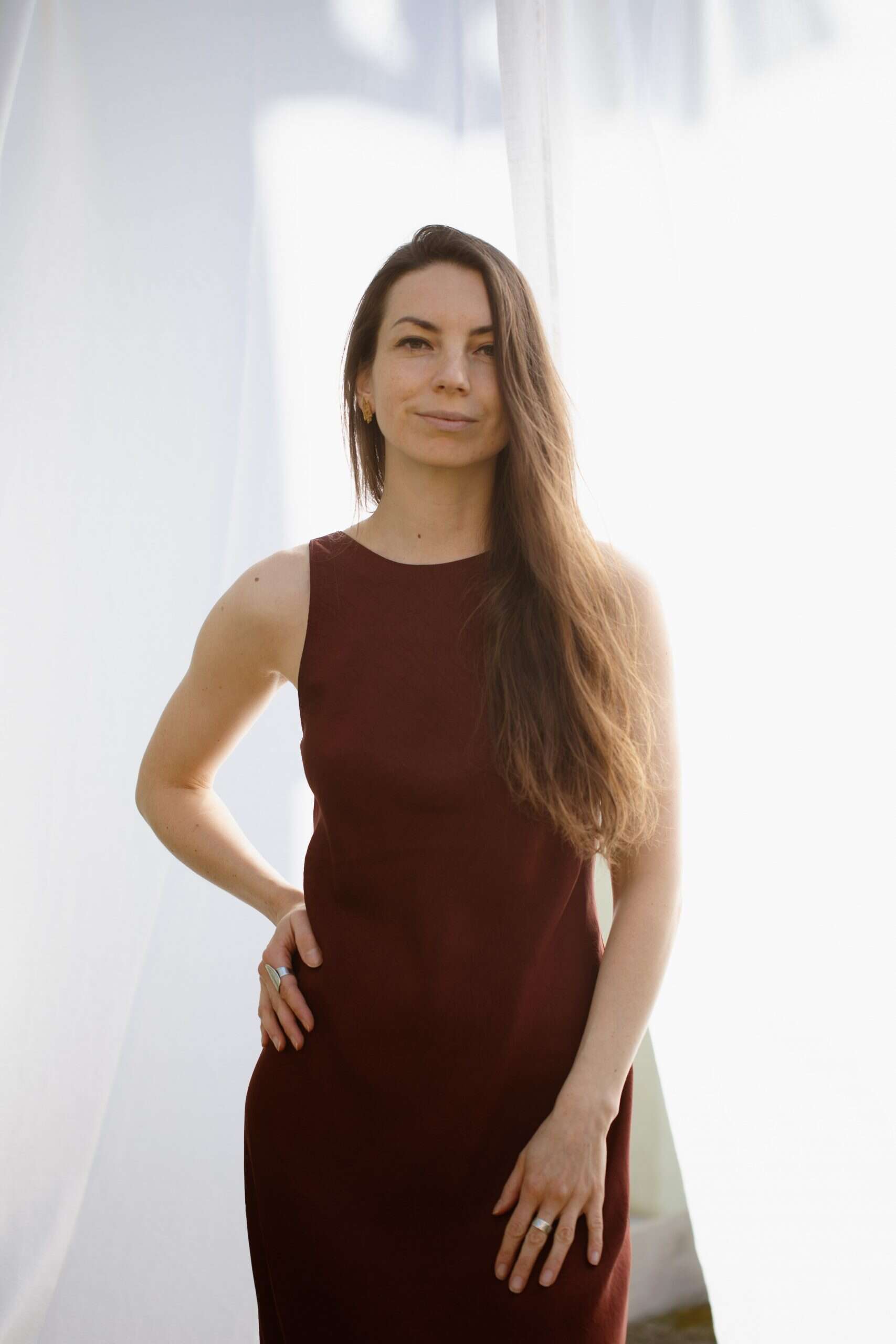 Elegant woman in a sleeveless maroon dress, standing confidently indoors.