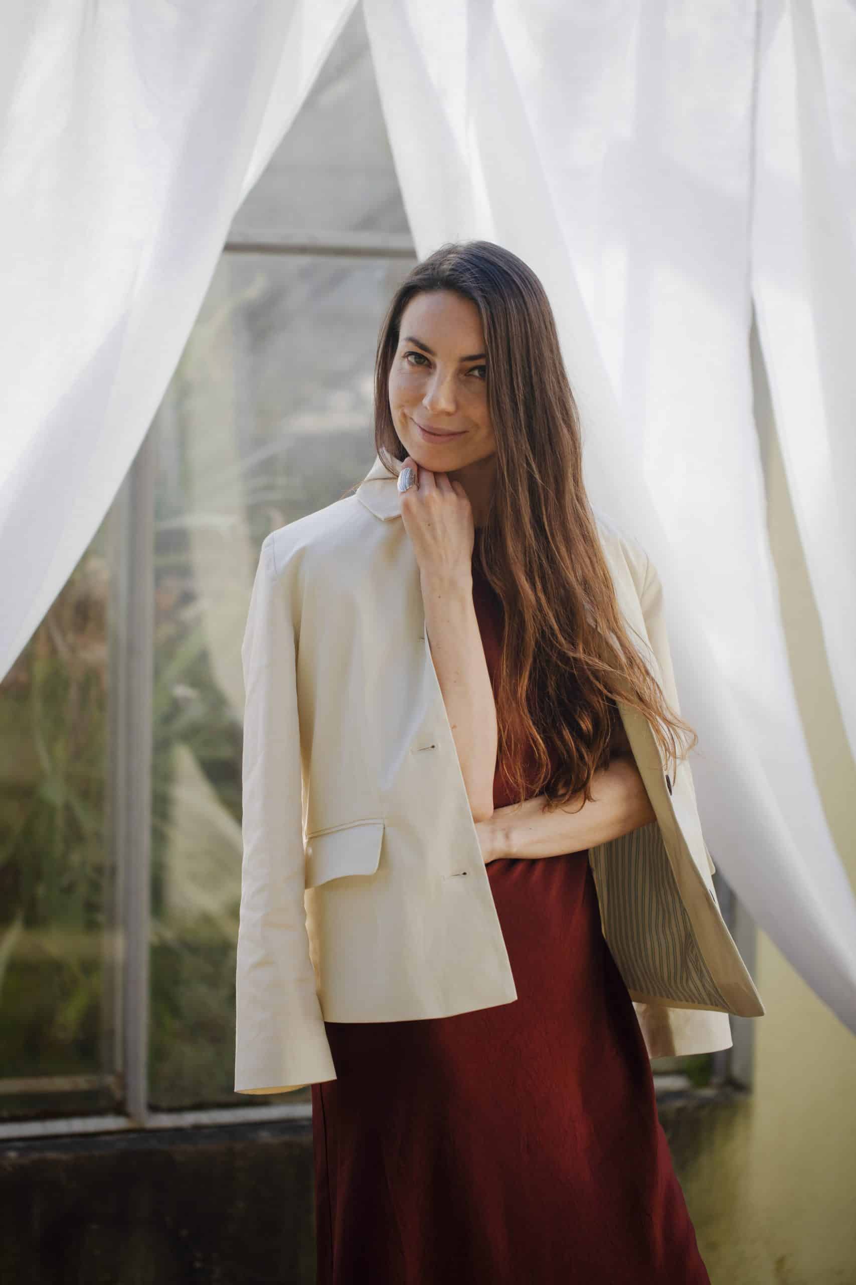 Elegant woman in a beige blazer and maroon dress for professional or fashion photoshoot.