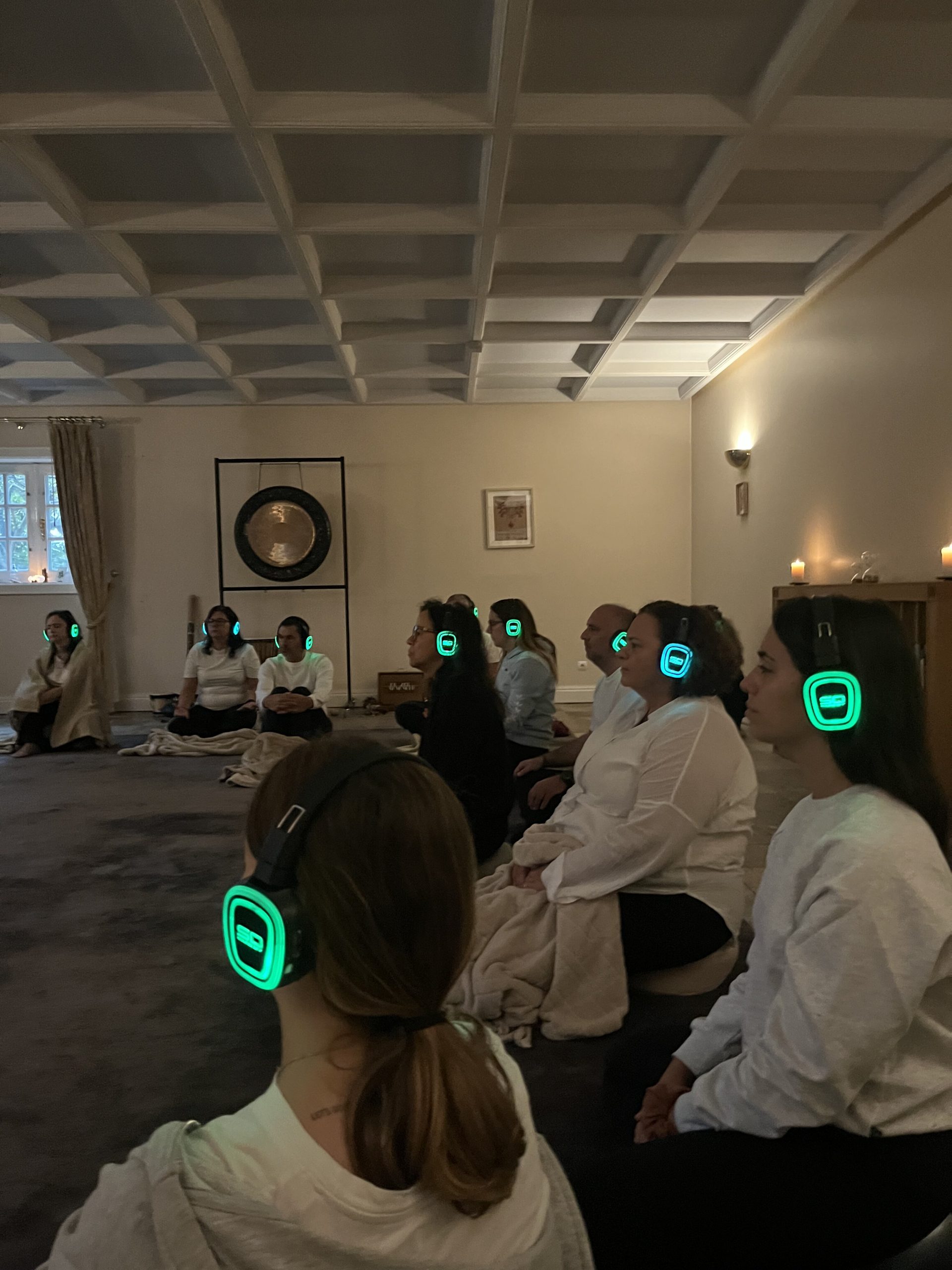 Comfortable meditation session with people wearing glowing headphones in tranquil indoor setting.