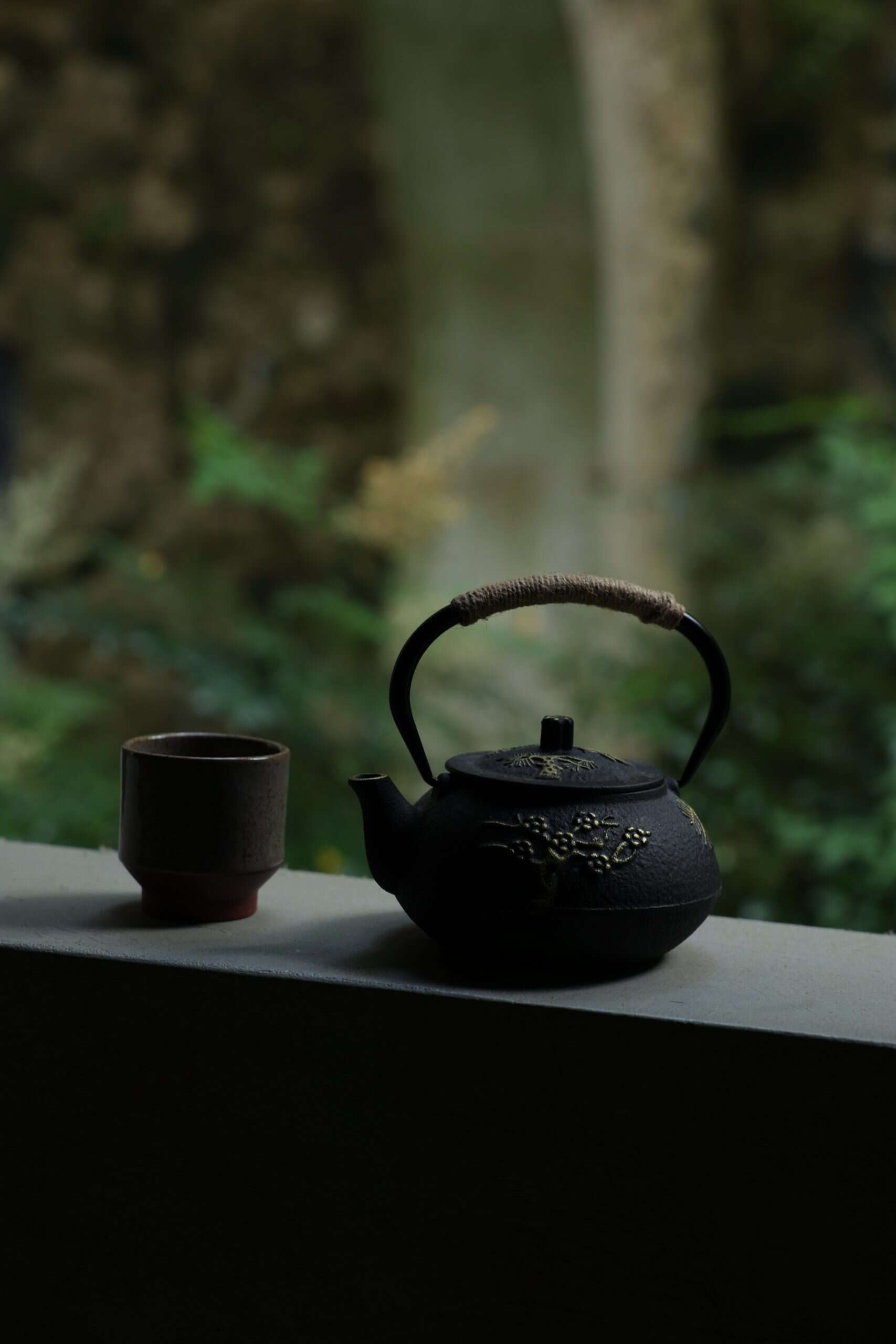 Black ceramic teapot and cup with floral design, serene outdoor setting, peaceful tea moment.