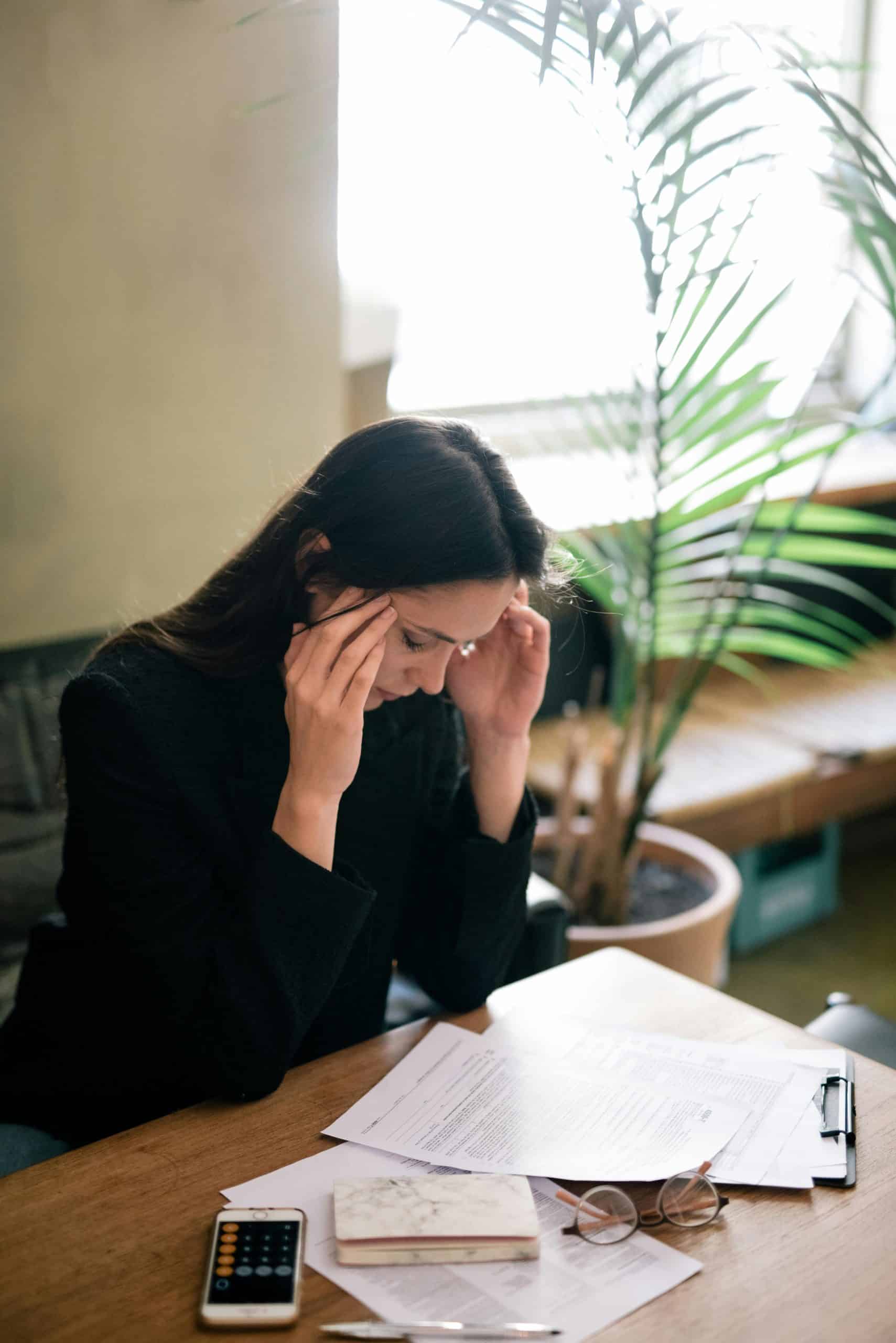 Stressed woman working on finances or documents at desk in cozy office environment.